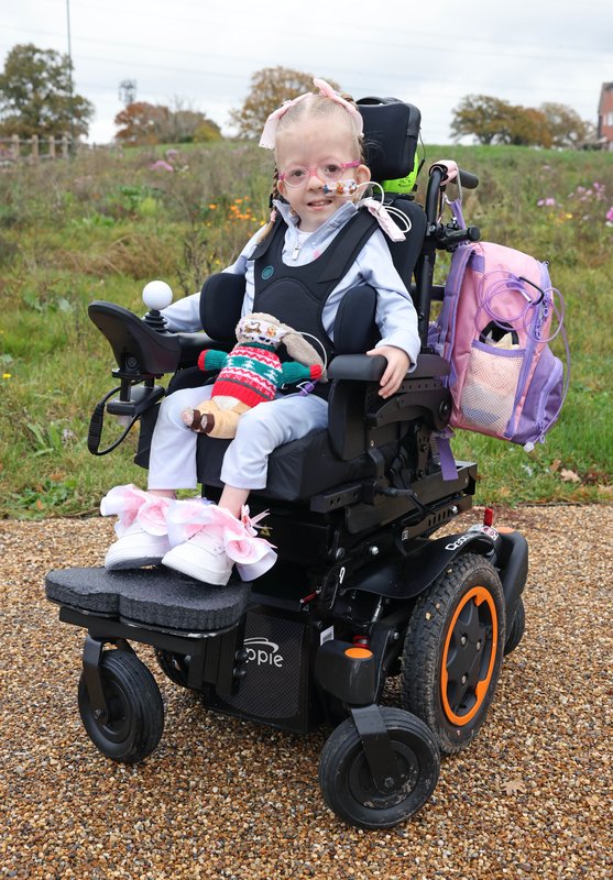 Harper sits proudly in her powered chair. She has her cuddly toy on her lap.