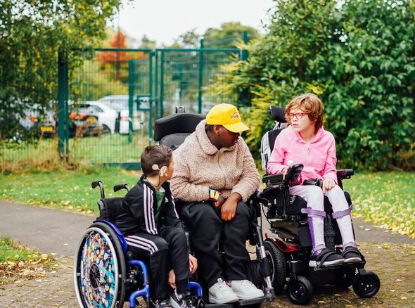 Three young wheelchair users are chatting in a park