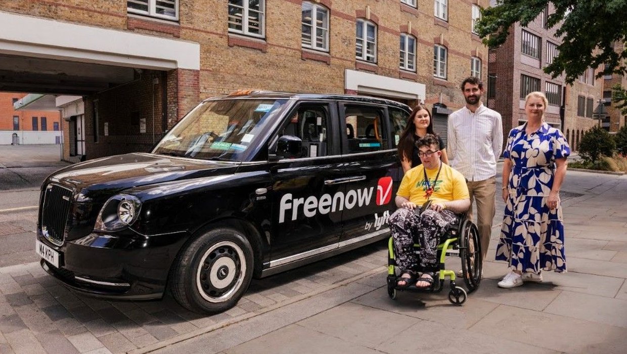 A group of people standing next to a black taxi with the Freenow by Lyft logo