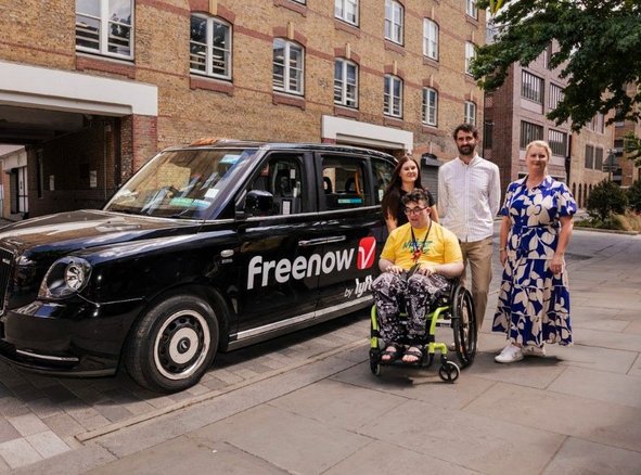 A group of people standing next to a black taxi with the Freenow by Lyft logo