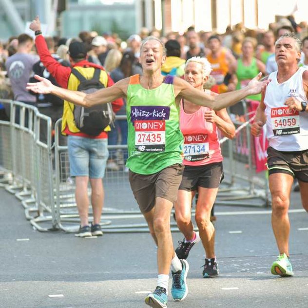 A runner in a green Whizz Kidz top holds his arms out as he soaks up the atmosphere
