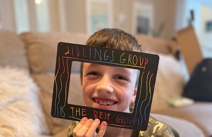 A child holds a frame in front of him that reads 'Sibling Group the best group'