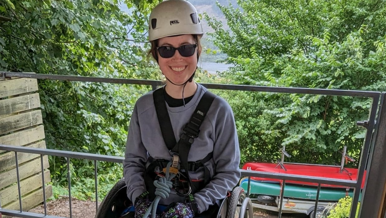 Rebecca from Kidz Board roped up and ready to abseil. She is in her wheelchair, wearing a white climbing helmet and sunglasses.