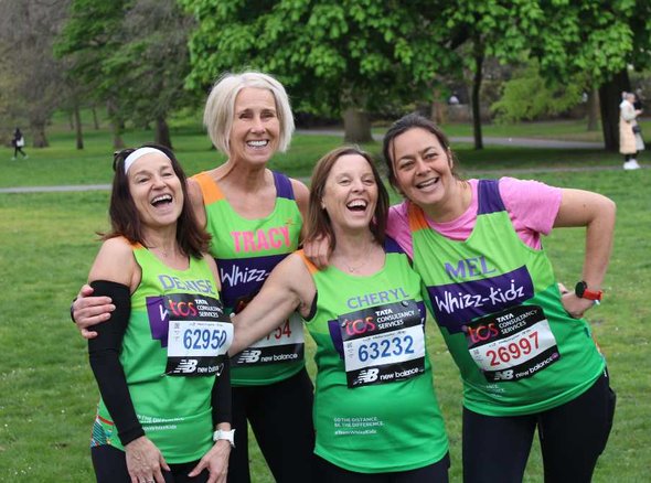 Four runners in green Whizz Kidz vests smile and laugh posing for a photo