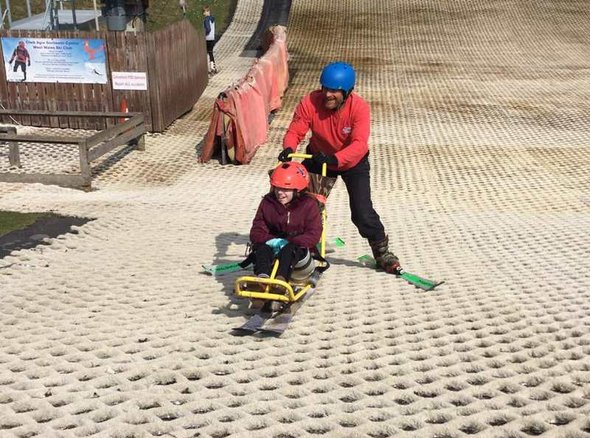 A young wheelchair user is pushed down a dry ski slope