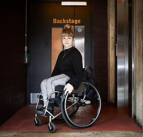 Portrait of Ruth Madeley. She is photographed in from of a door saying Stage Door.