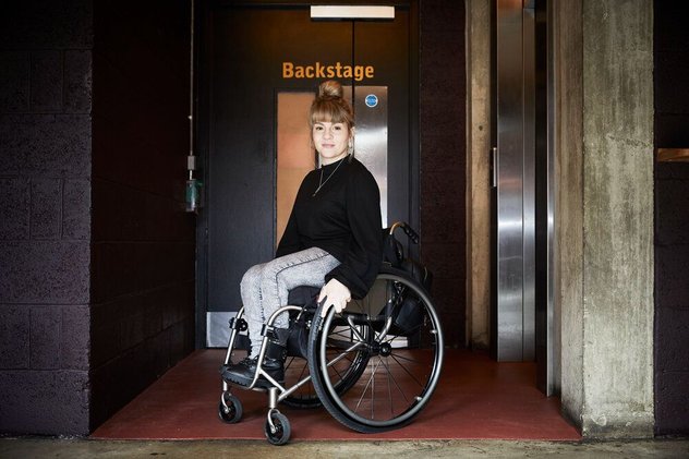Portrait of Ruth Madeley. She is photographed in from of a door saying Stage Door.