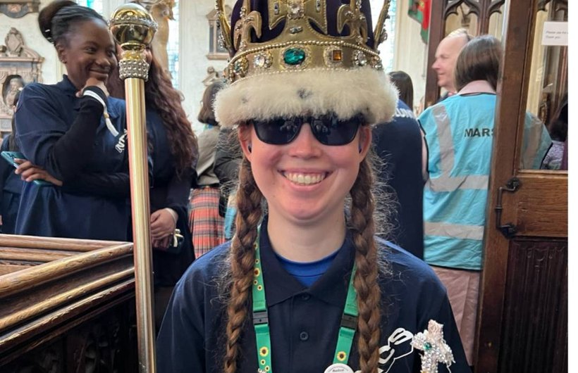 Rebecca wearing a bejewelled crown, holding an orb and sceptre. She has dark glasses and is smiling.