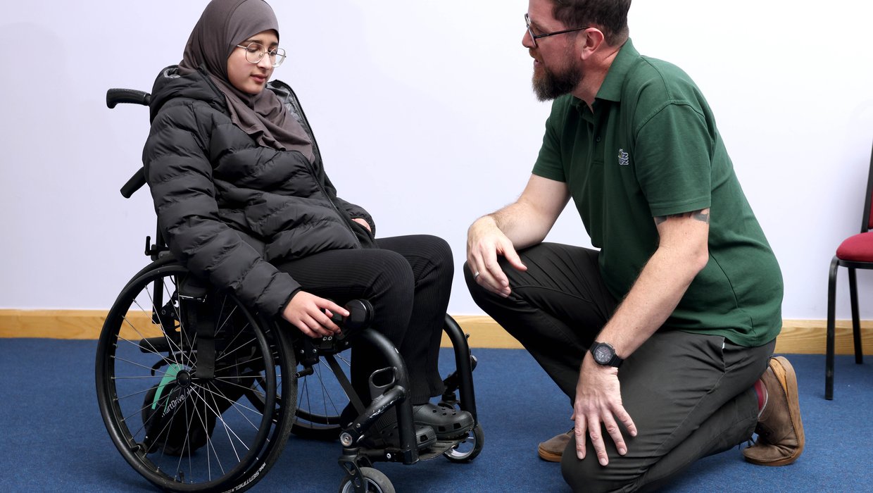 Sophia, a teenage girl who wears a hijab, sits in her wheelchair talking to a member of the Whizz Kidz team