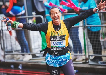 A runner in a yellow Whizz Kidz vest waves to a Whizz Kidz cheer point