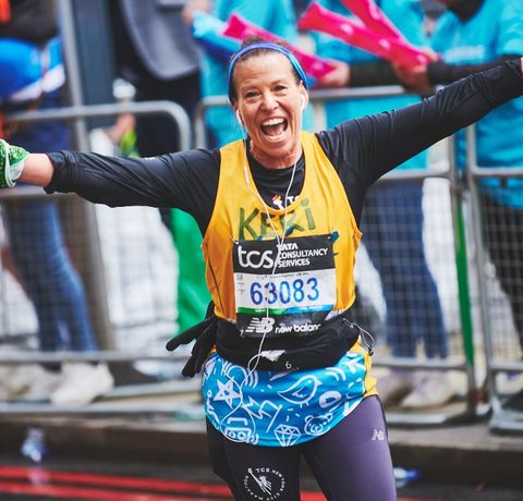 A runner in a yellow Whizz Kidz vest waves to a Whizz Kidz cheer point