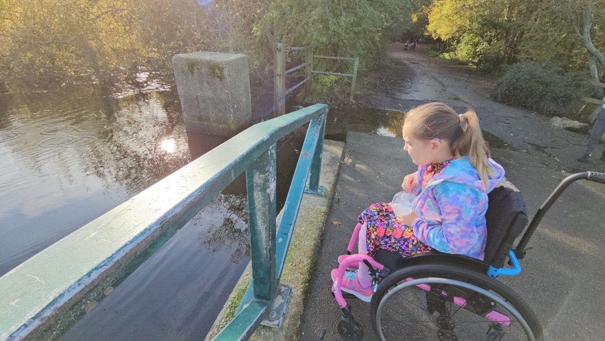 A young wheelchair user sits by the side of a lake