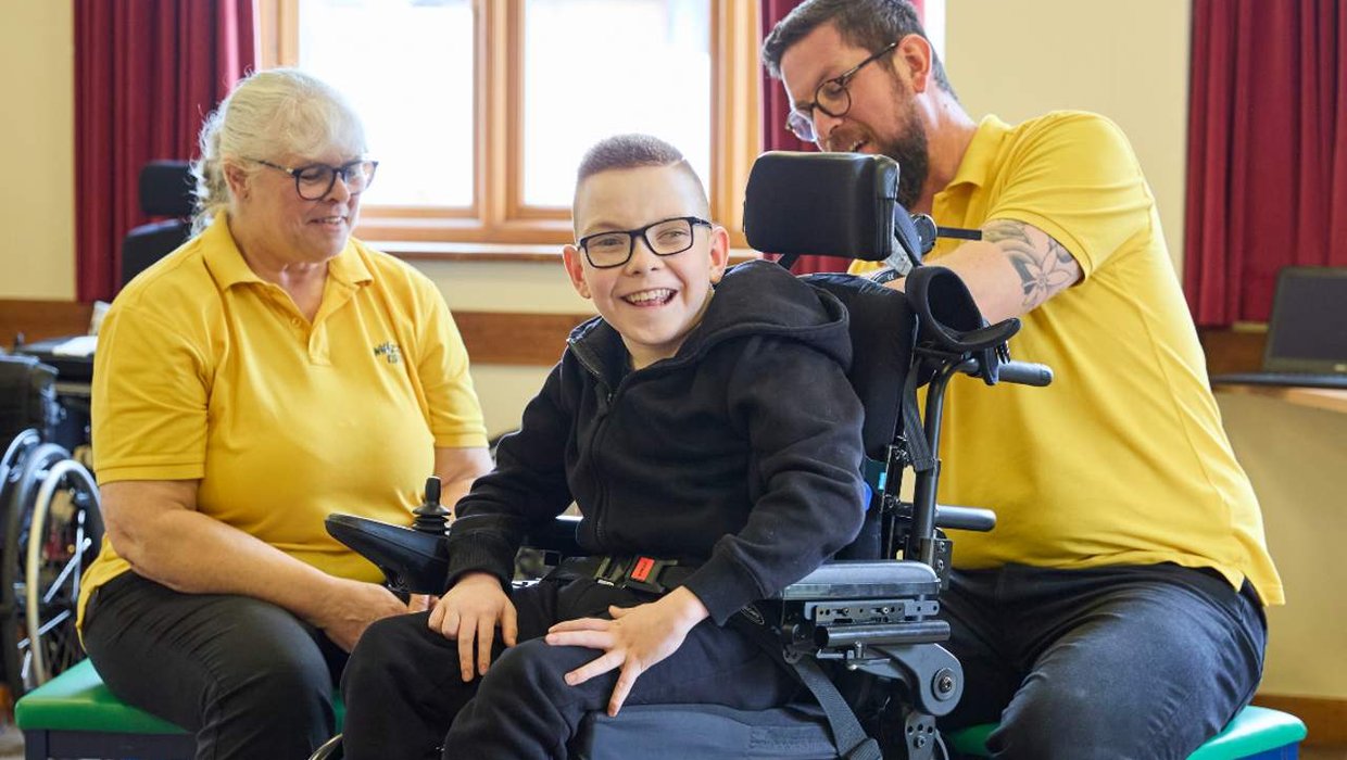 Engineer John Bearman adjusts Logan's wheelchair as he's had another growth spurt, while Sarah looks on Engineer John Bearman adjusts Logan's wheelchair as he's had another growth spurt, while Sarah looks on