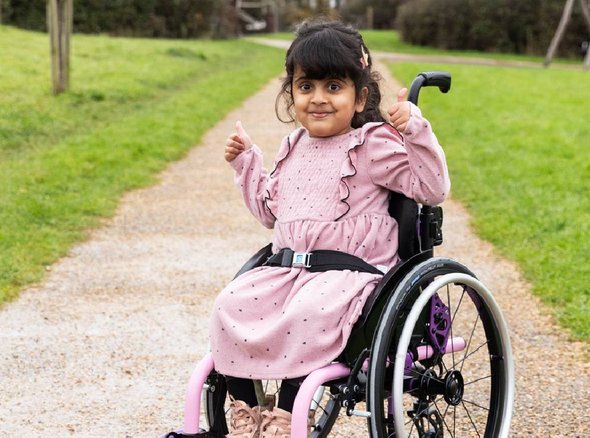 Aniyah outside in her new wheelchair from Whizz KIdz. She is giving a thumbs up and smiling at the camera.