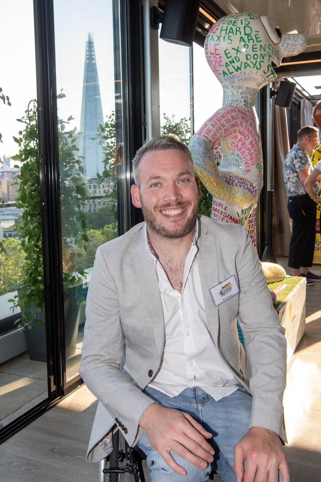 Martin Dougan sits in front of a Morph statue wearing a smart jacket and jeans