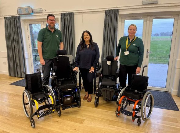 Sonal from The Barratt Foundation in the middle of two Whizz Kidz therapists, standing in front of four wheelchairs