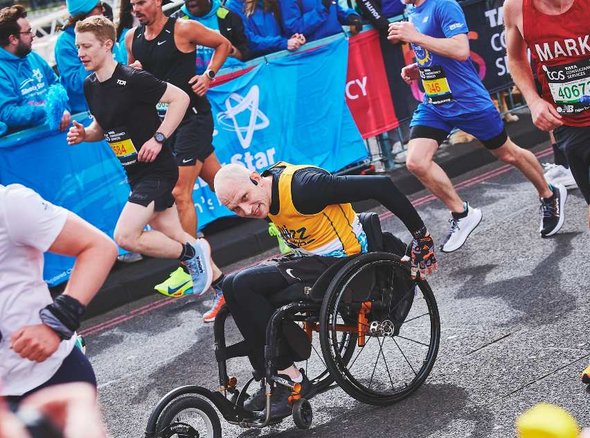 A wheelchair user in a Whizz Kidz vest pushes his wheelchair along the London Marathon course